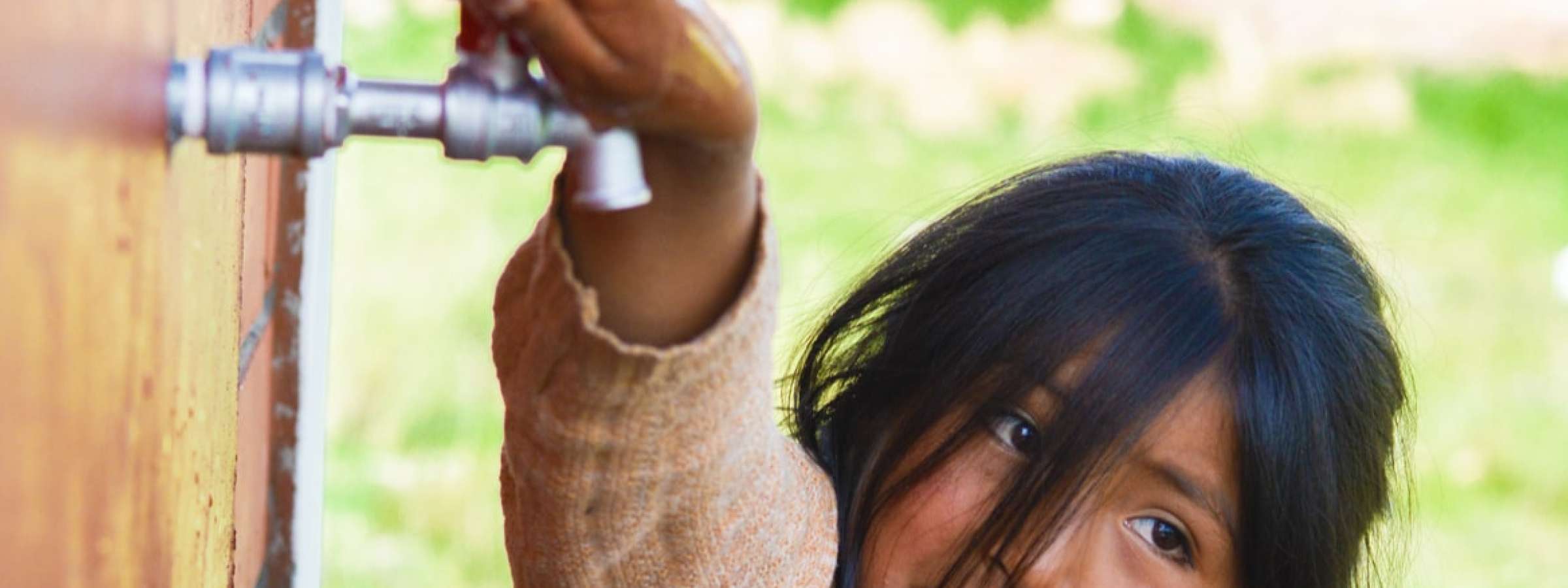 A little girl trying to open a water tap in Mexico.