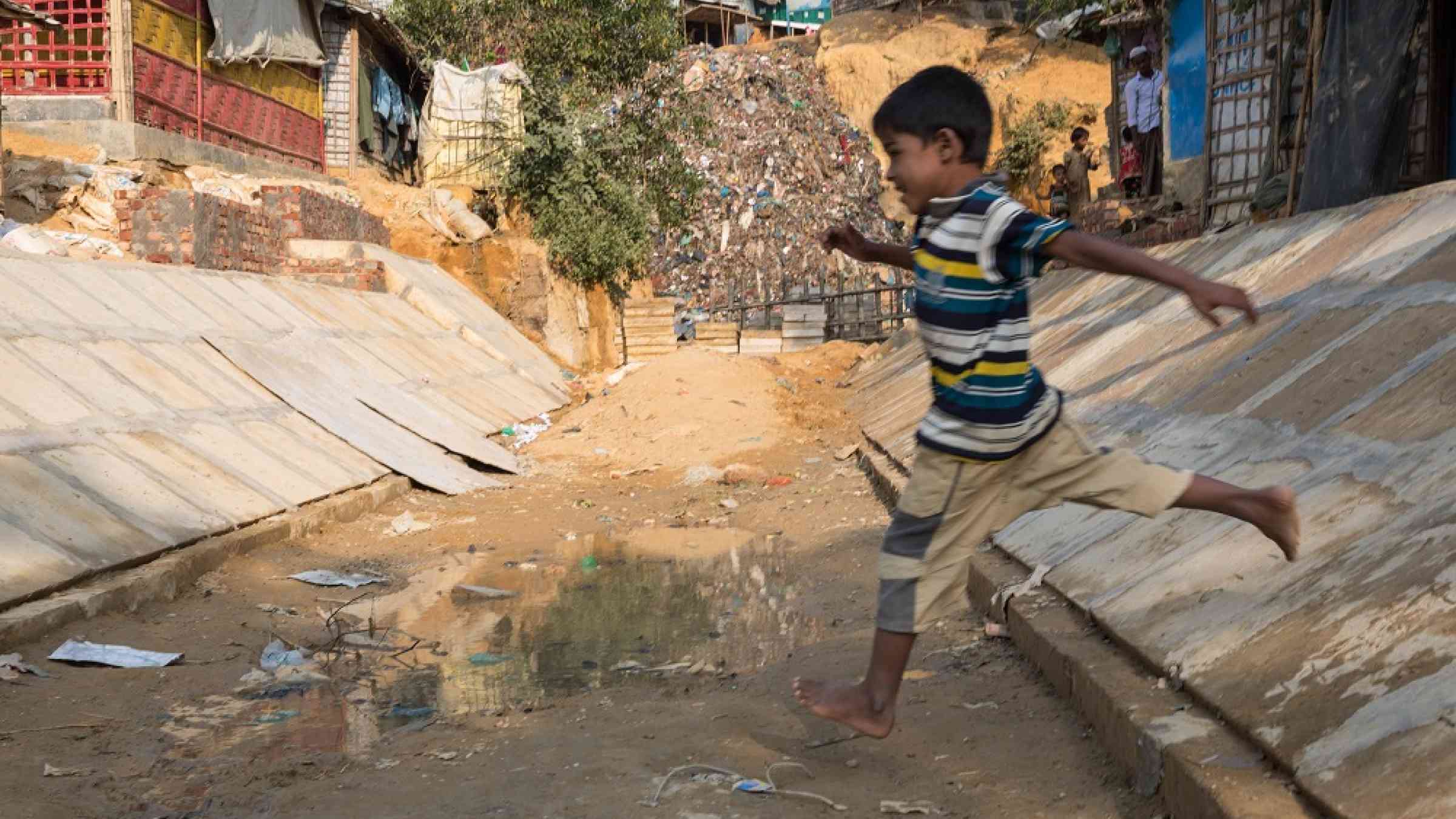 Child leaps over a drain in a camp in Bangladesh